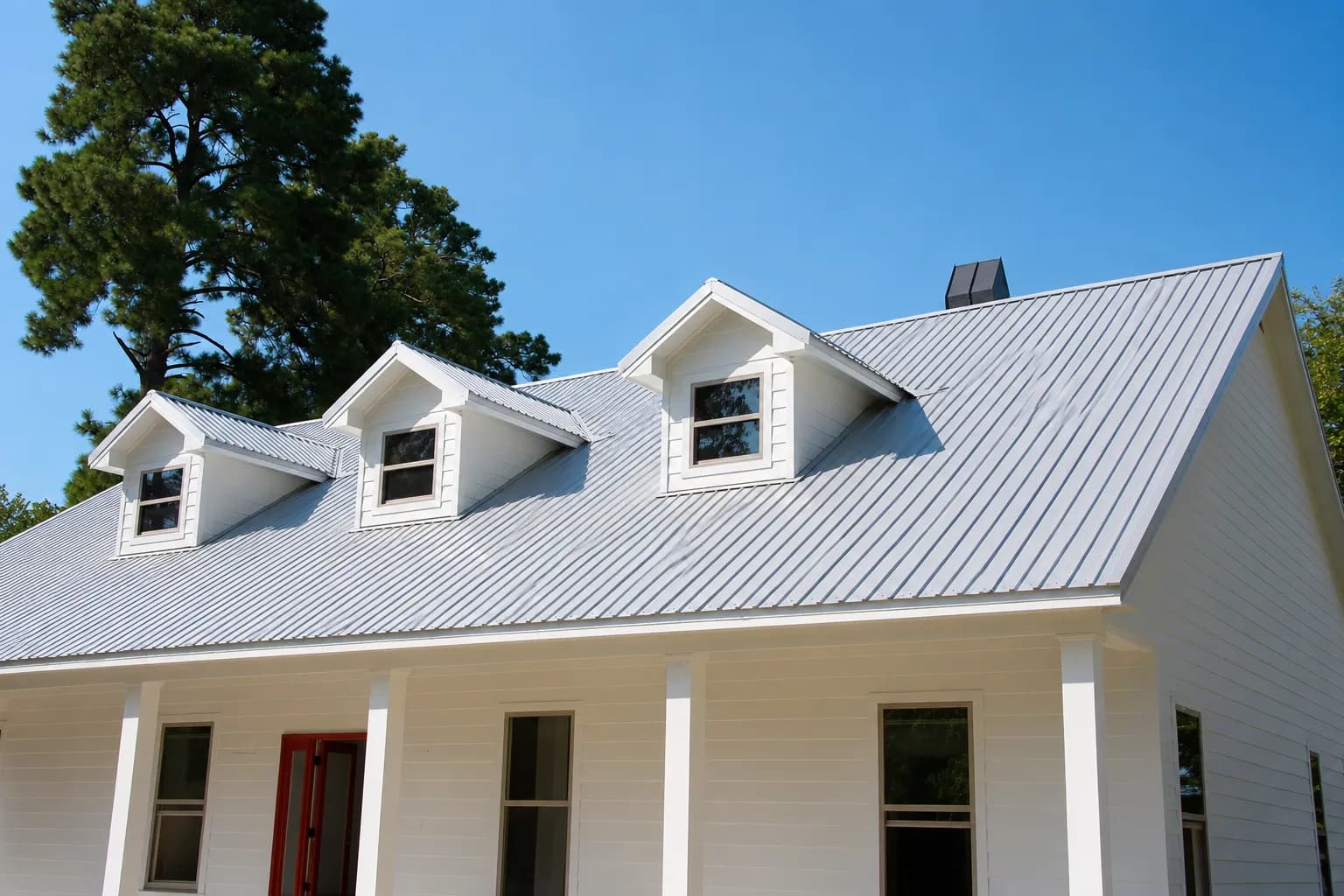 A silver standing-seam metal roof on a white farmhouse with dormers
